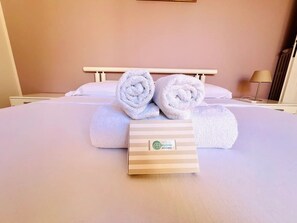Ett hotellrum med en säng, två hoprullade handdukar och en handduksförvaringslåda med hotellets logotyp.