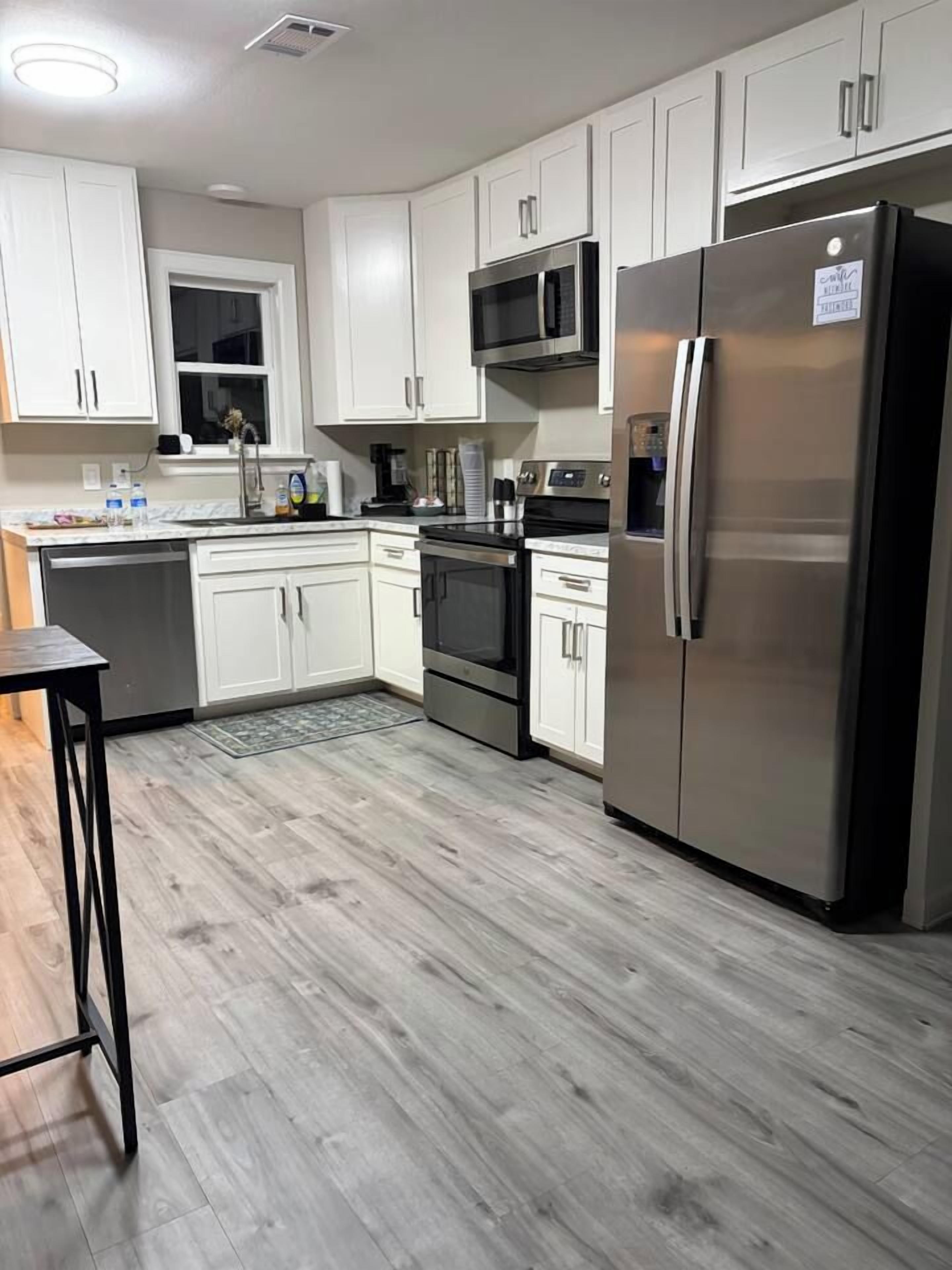 A modern kitchen with white cabinets, stainless steel appliances, and a wooden floor.