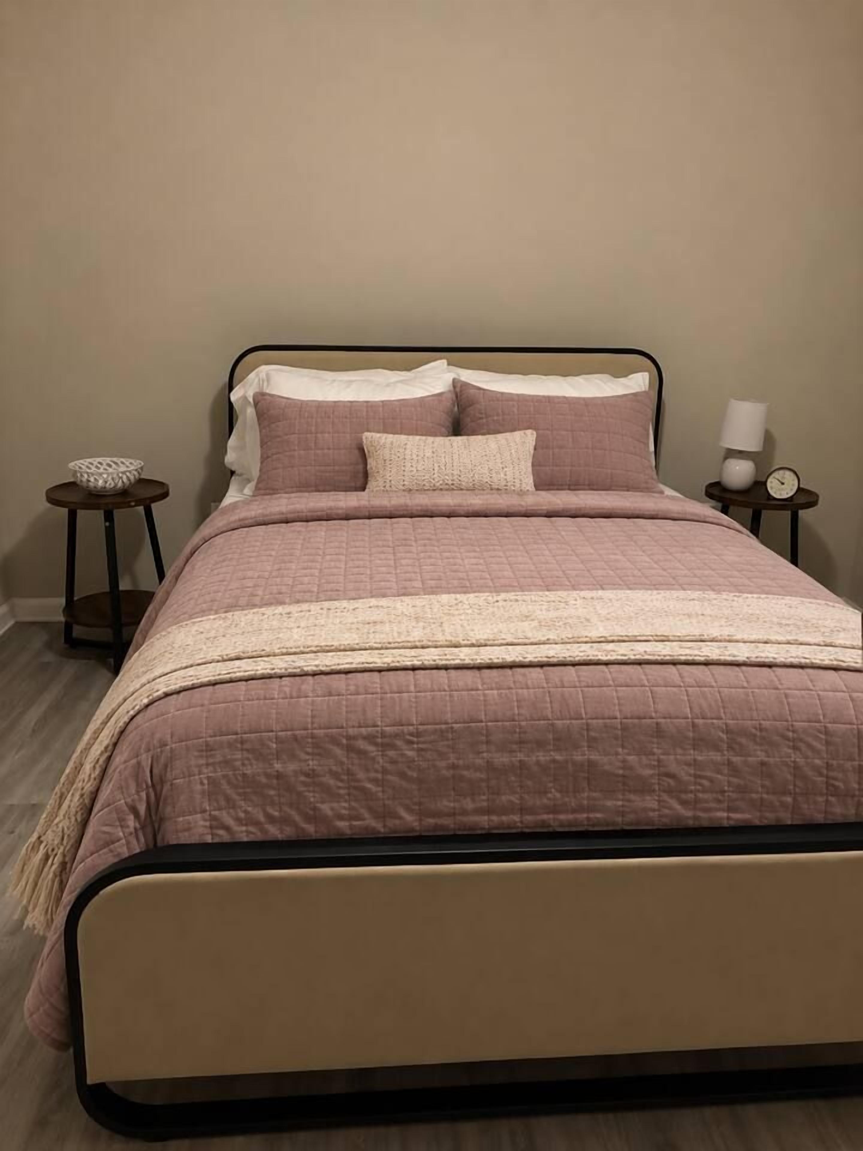 A bed with a headboard, a bedside table with a lamp, and a small table with a basket.