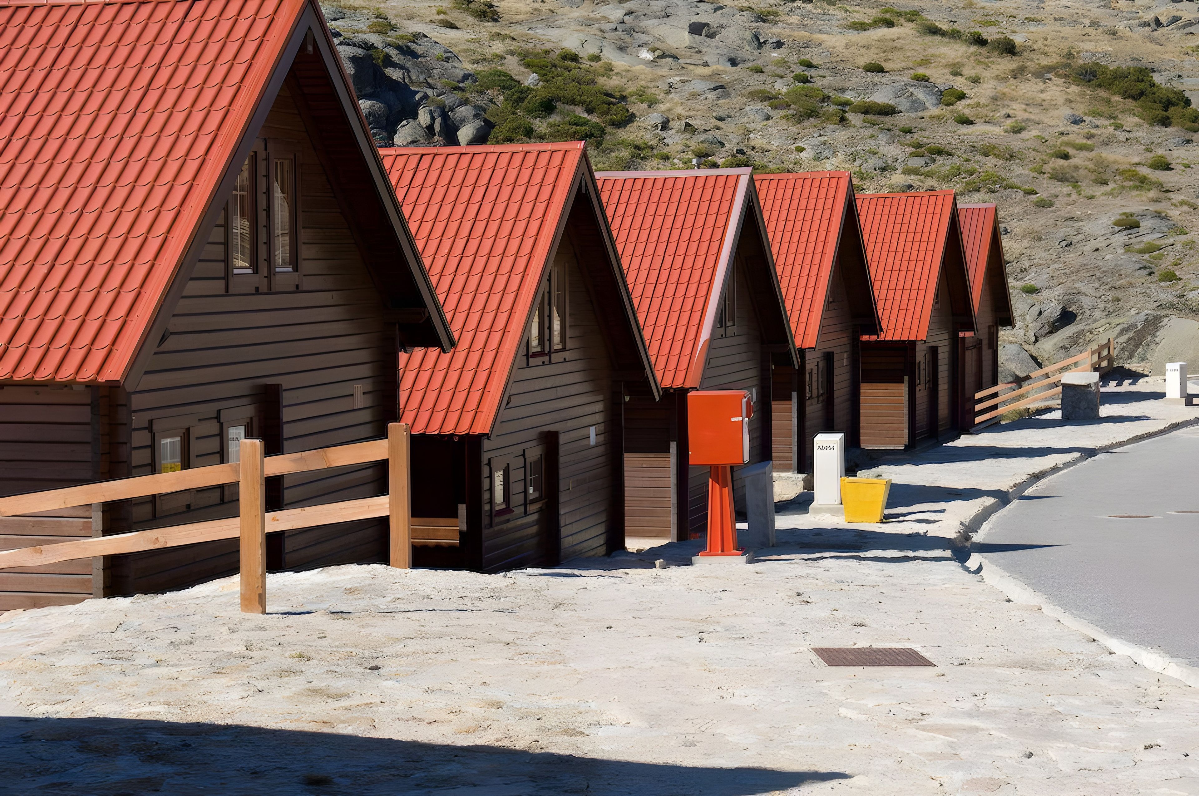 Een rij houten hutten met rode daken, elk met een klein terrasje en een deur.