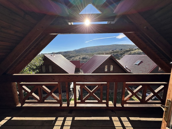 Un balcón de madera con vista a casas vecinas y un cielo despejado.