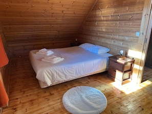 Una habitación con paneles de madera, una cama, almohadas, una mesita de noche con una lámpara y una alfombra redonda.