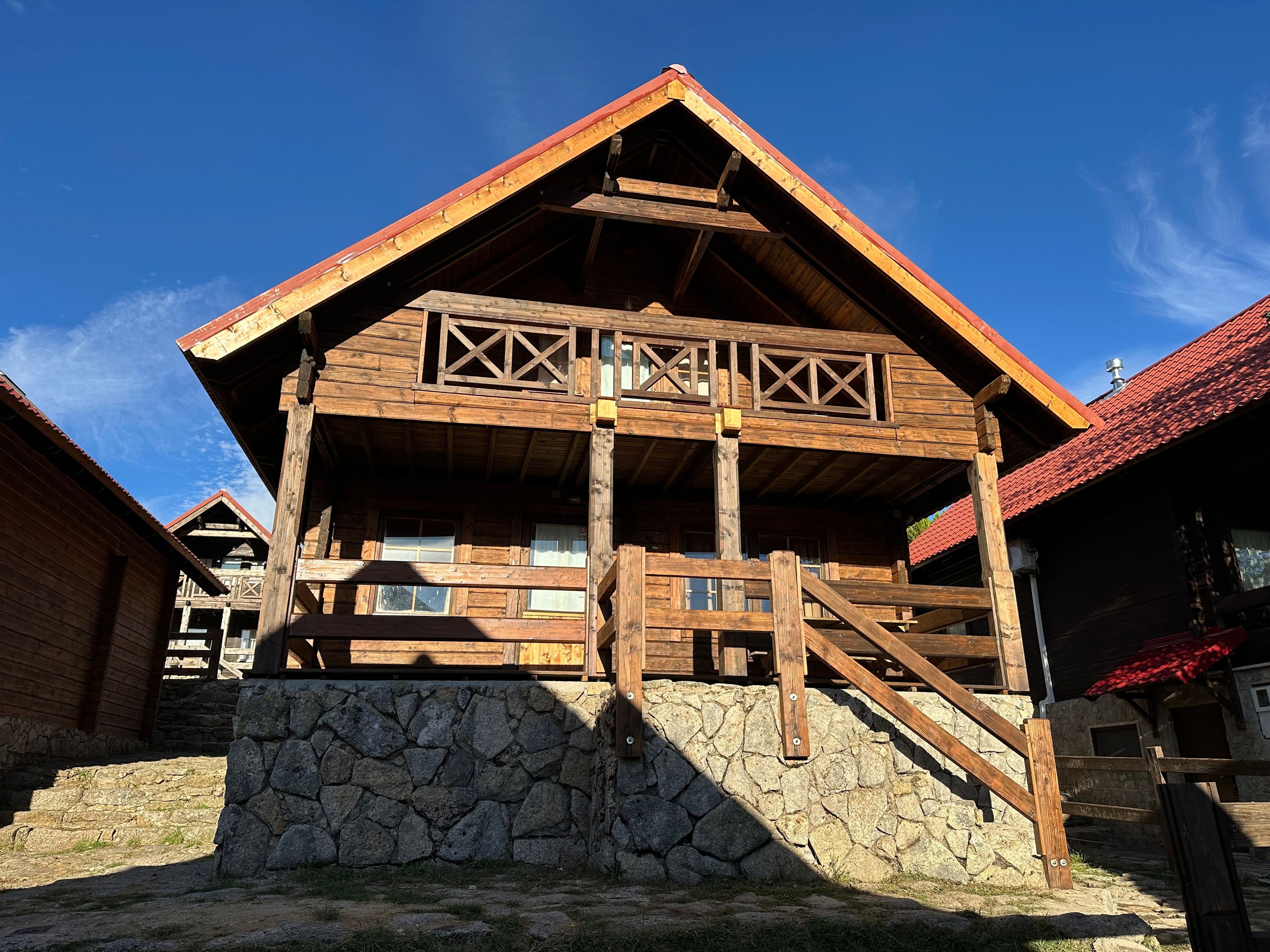 Un edificio de madera con cimientos de piedra, una escalera de madera y un balcón con barandillas.