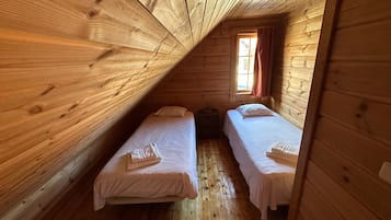 A cabin with two beds, wooden walls, a sloped ceiling, and a window with curtains.