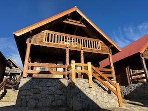 Una cabaña de madera con cimientos de piedra, escaleras de madera y un balcón.