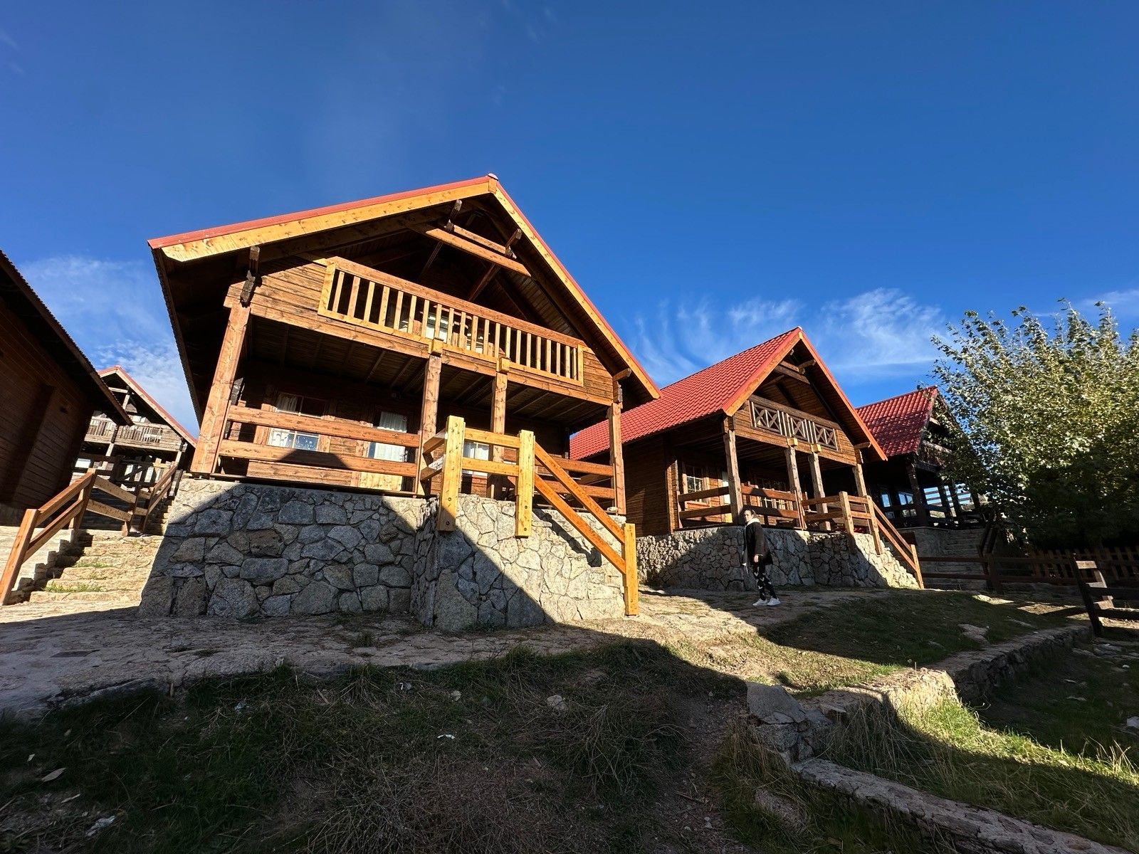 Een houten chalet met een stenen fundering, houten balkons en een dak met rode tegels.