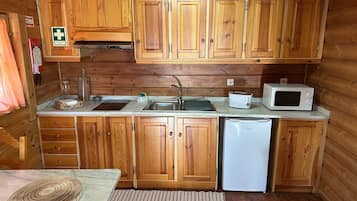 Eine kleine Küche mit Holzausstattung, einer Spüle, einem Toaster, einer Mikrowelle und einem Kühlschrank.