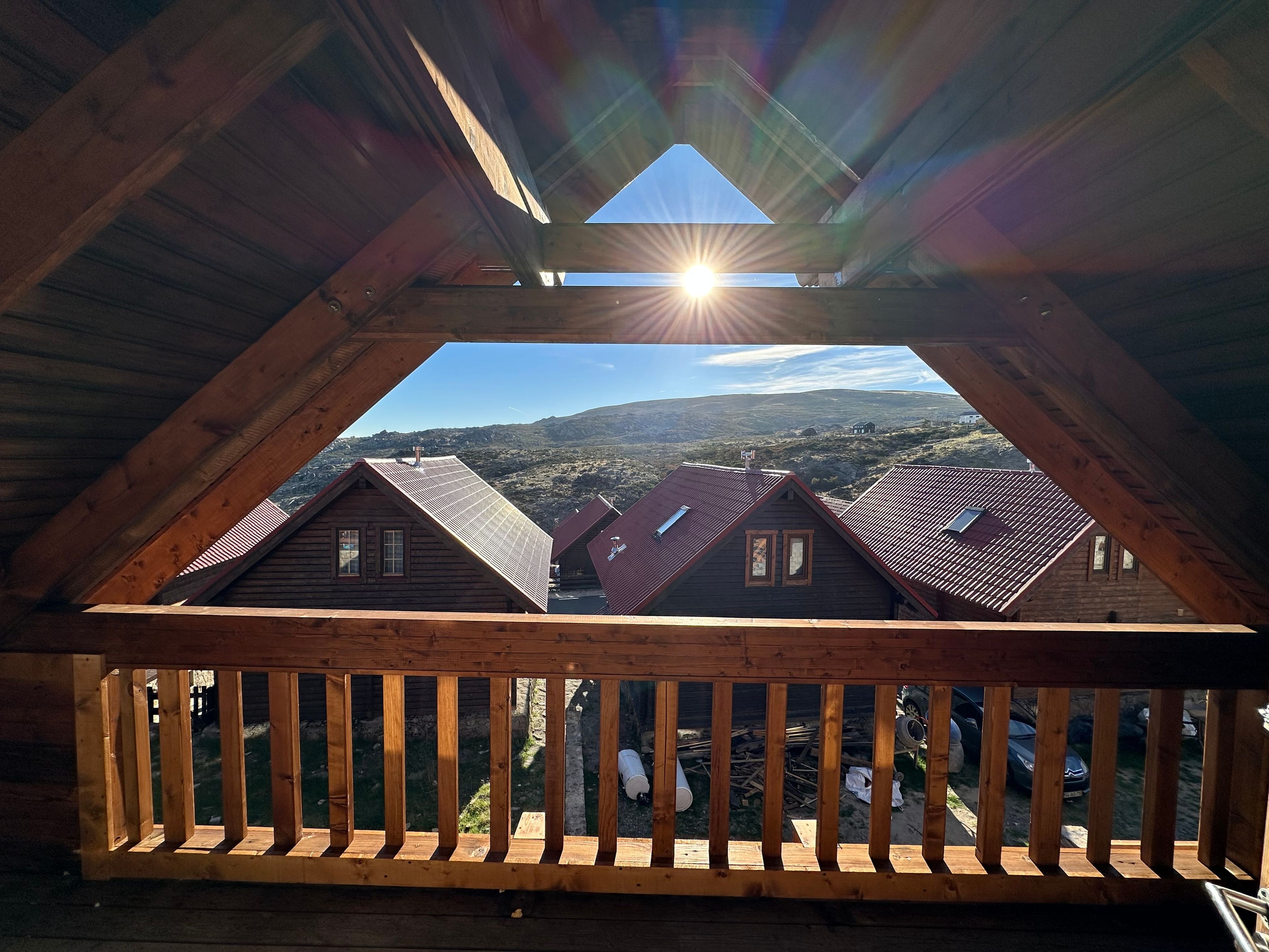 Een houten balkon met uitzicht op een glooiend landschap en verschillende gebouwen.