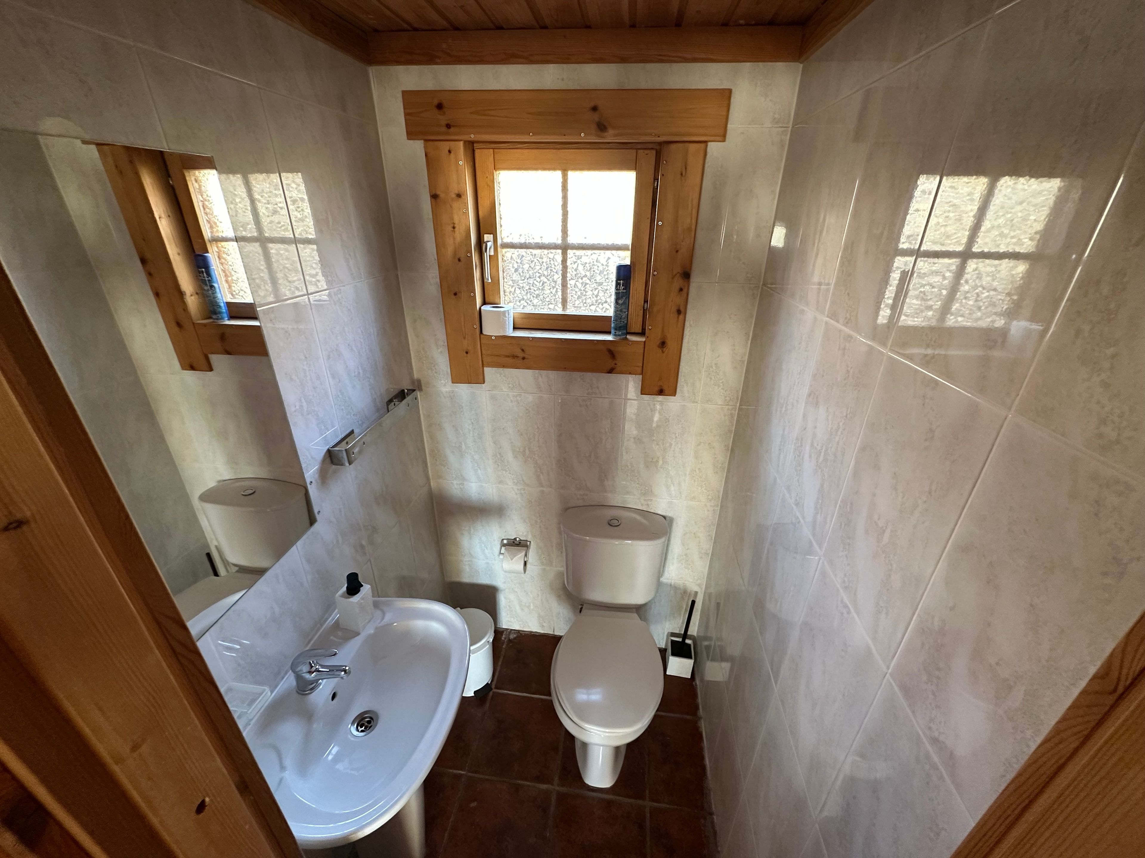 Ein kleines Badezimmer mit Holzfenster, Waschbecken und zwei Toiletten.