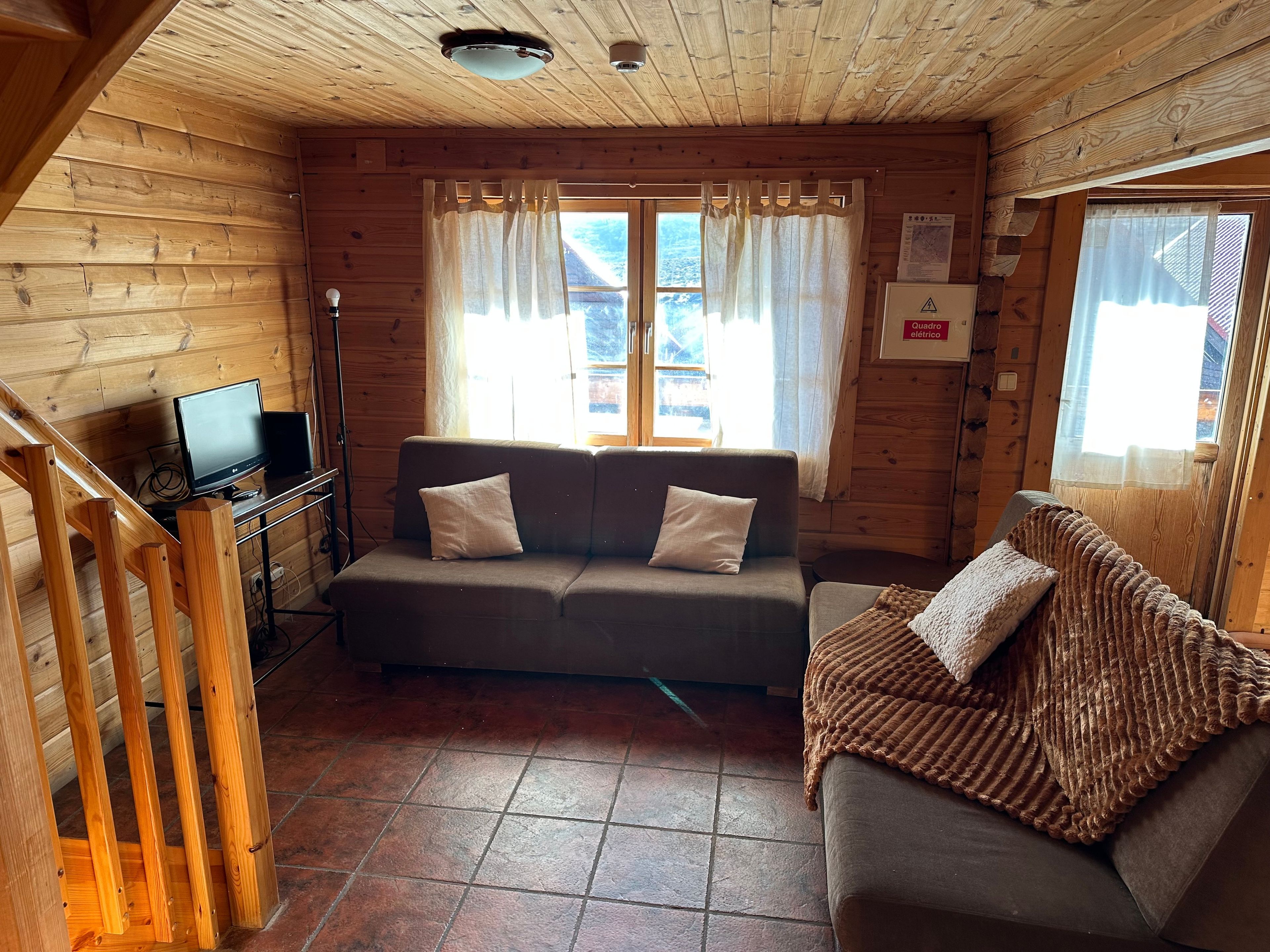 Ein Holzblockhaus-Innenraum mit einer Couch, einem Fernseher und einem Fenster mit Vorhängen.