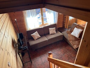Interior de una cabaña de madera con un sofá, una mesita y una ventana.