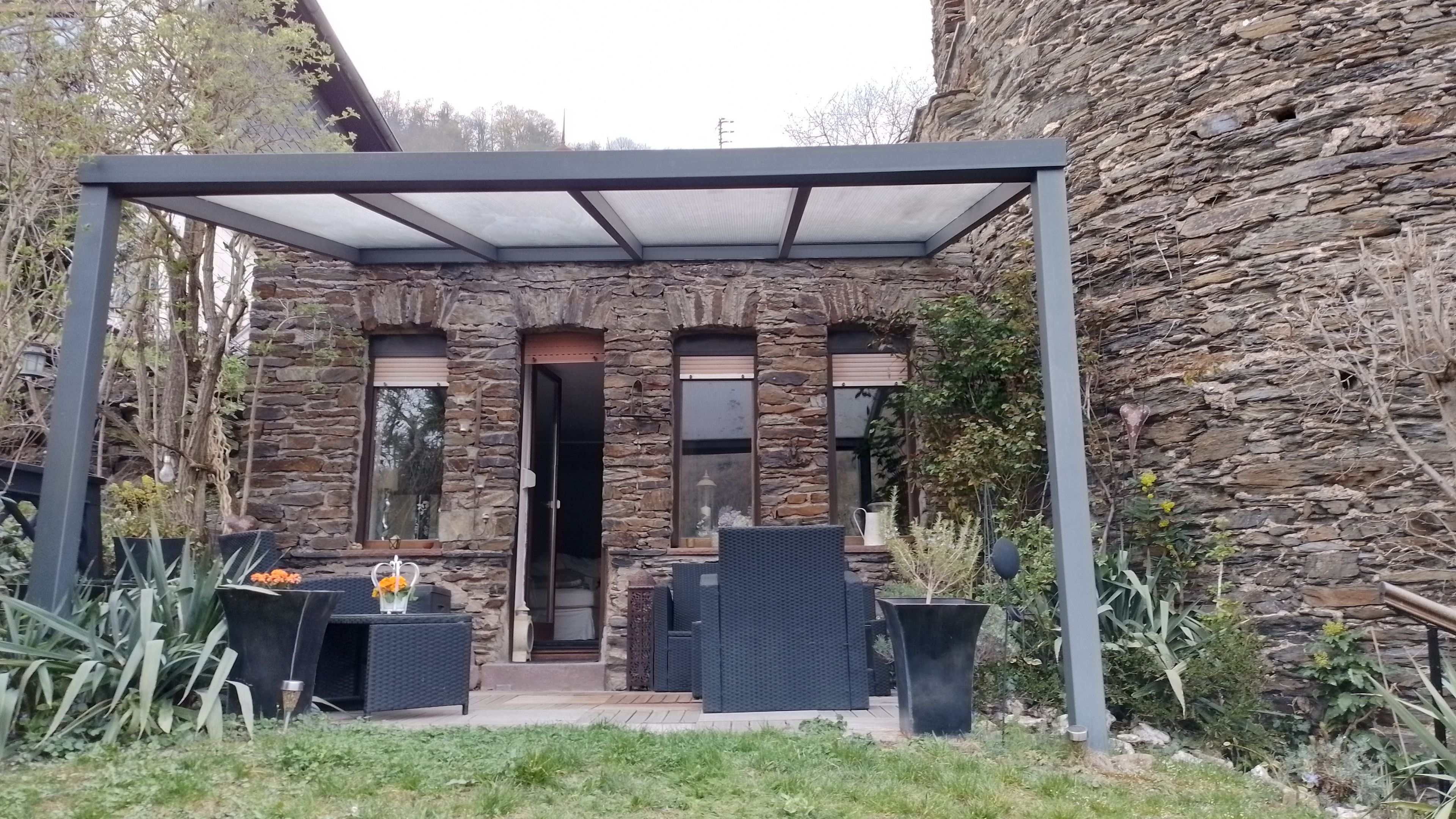 Ein überdachter Patio-Bereich mit Steinmauern, Gartenmöbeln und Blick auf ein Steinhaus.