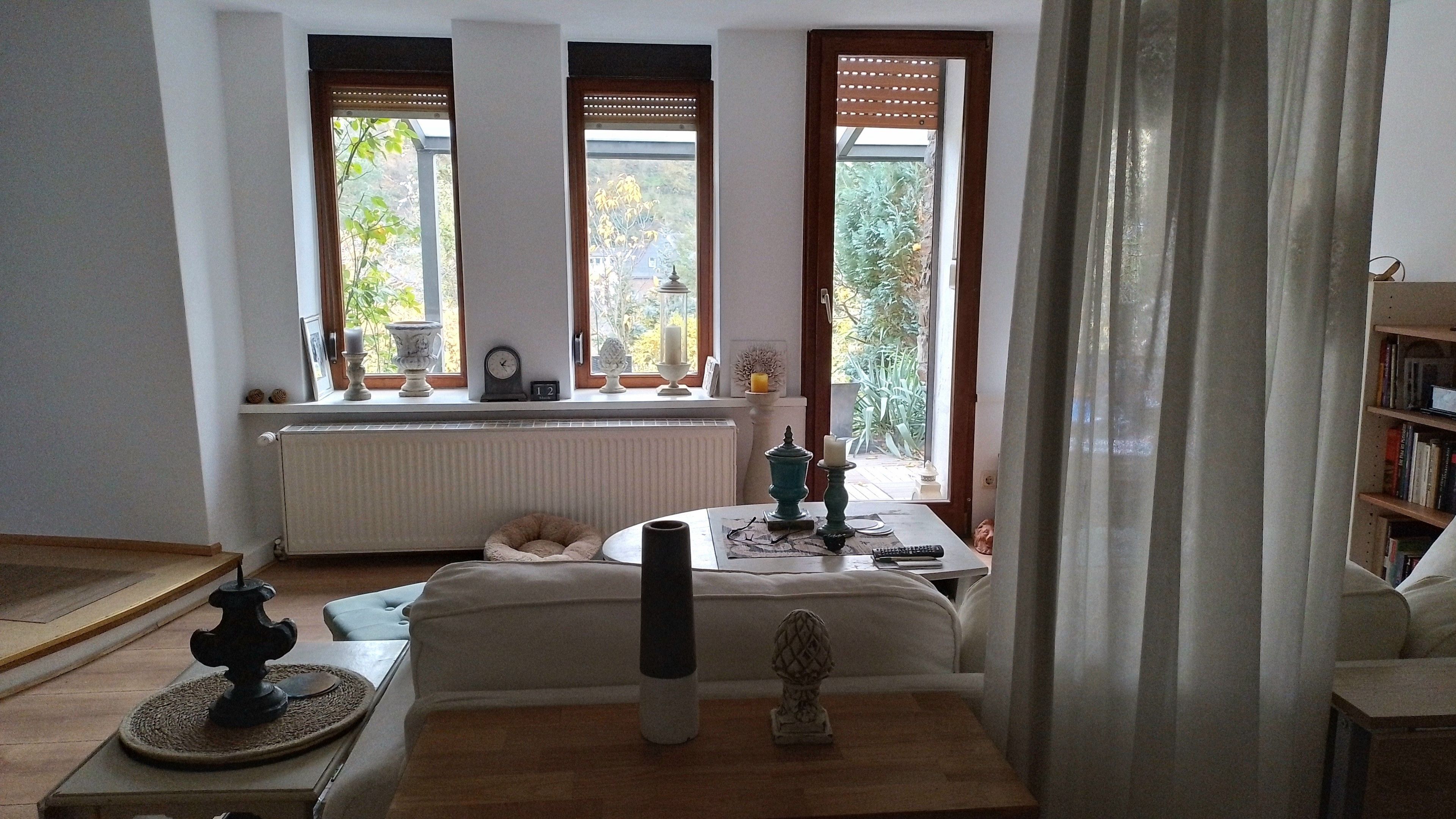 A room with a sofa, a table with a candle, a clock, and a view of greenery through windows.