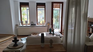 Una habitación con un sofá, una mesa con una vela, un reloj y vistas a zonas verdes a través de las ventanas.