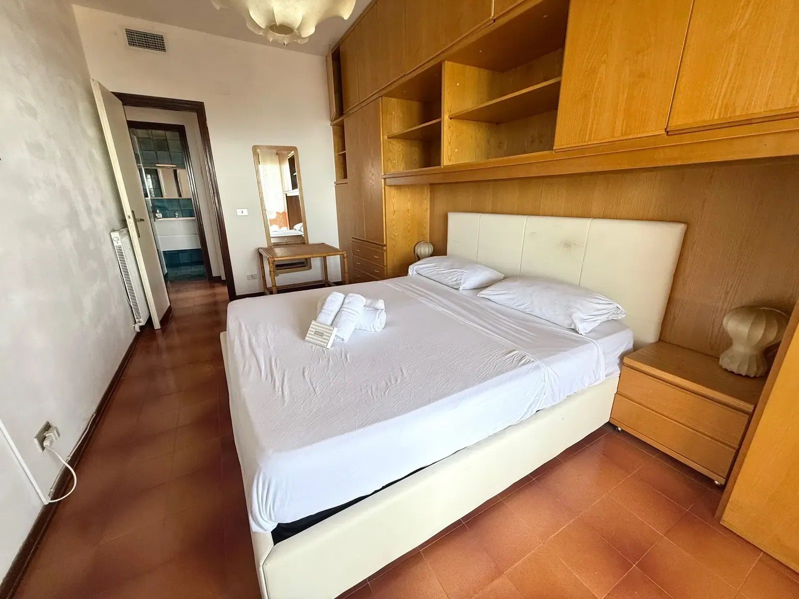 A hotel room with a large bed, wooden headboard, and built-in shelving.