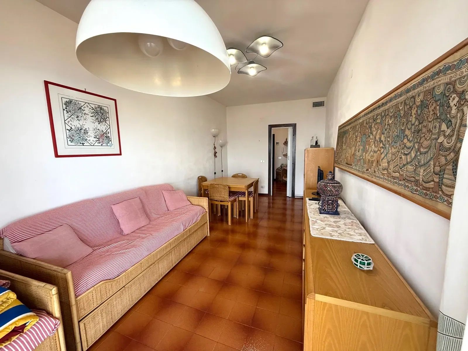 A living room with a sofa, a dining table with chairs, a wooden cabinet, and a large decorative tapestry.