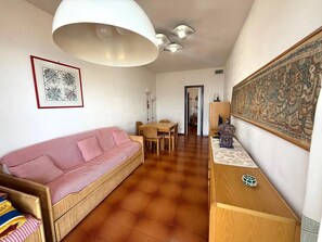 A living room with a sofa, a dining table with chairs, a wooden cabinet, and a large decorative tapestry. - New Listing (Sanremo)