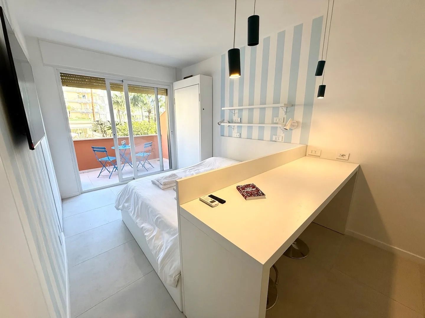Et moderne hotelværelse med en hvid seng, et skrivebord og en balkon med bord og stole.