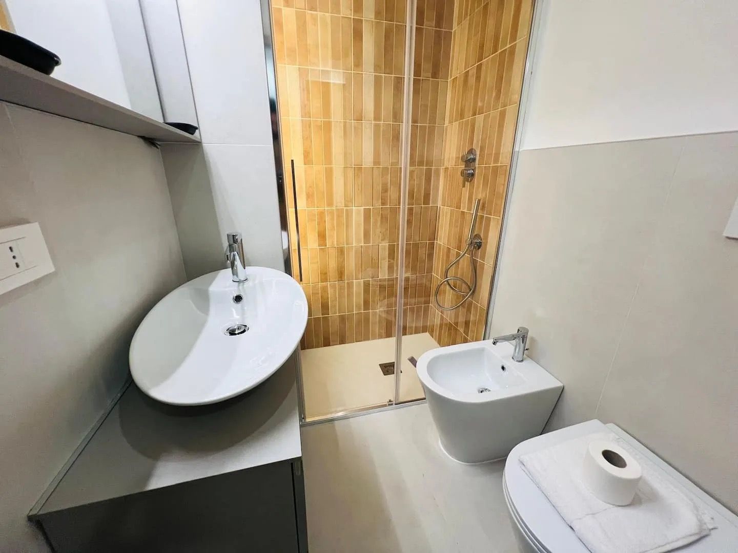 Et badeværelse med en hvid vask, en bidet og en bruseniche med glasdør.