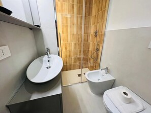 Et badeværelse med en hvid vask, en bidet og en bruseniche med glasdør.