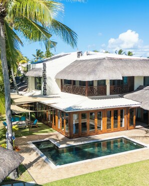 Un complexe hôtelier doté d’une piscine, de bâtiments à toits de chaume et situé dans un cadre tropical.