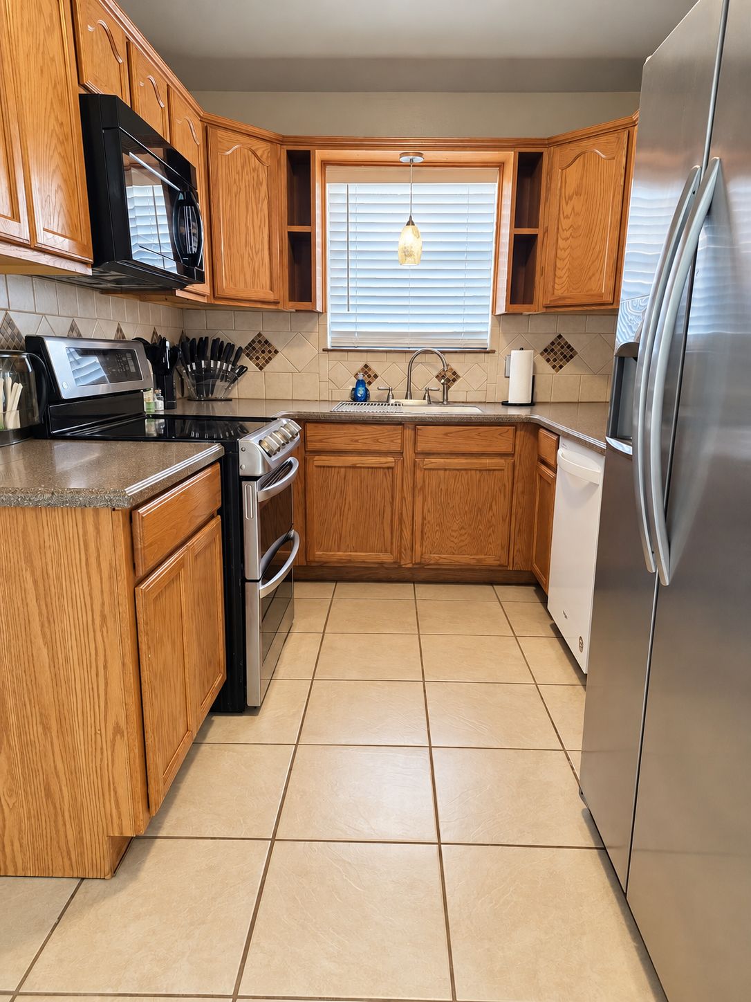 A kitchen with wooden cabinets, a stainless steel refrigerator, a microwave, and a stove.