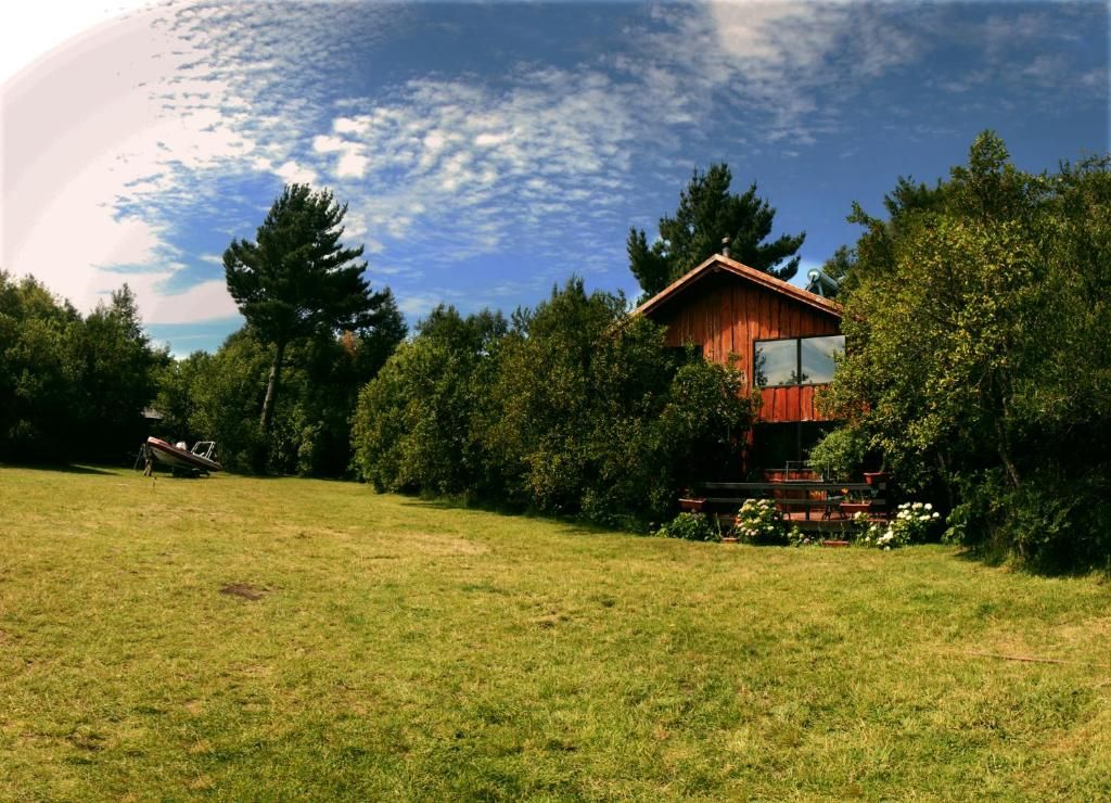 A wooden cabin with a deck, surrounded by trees and a grassy field.