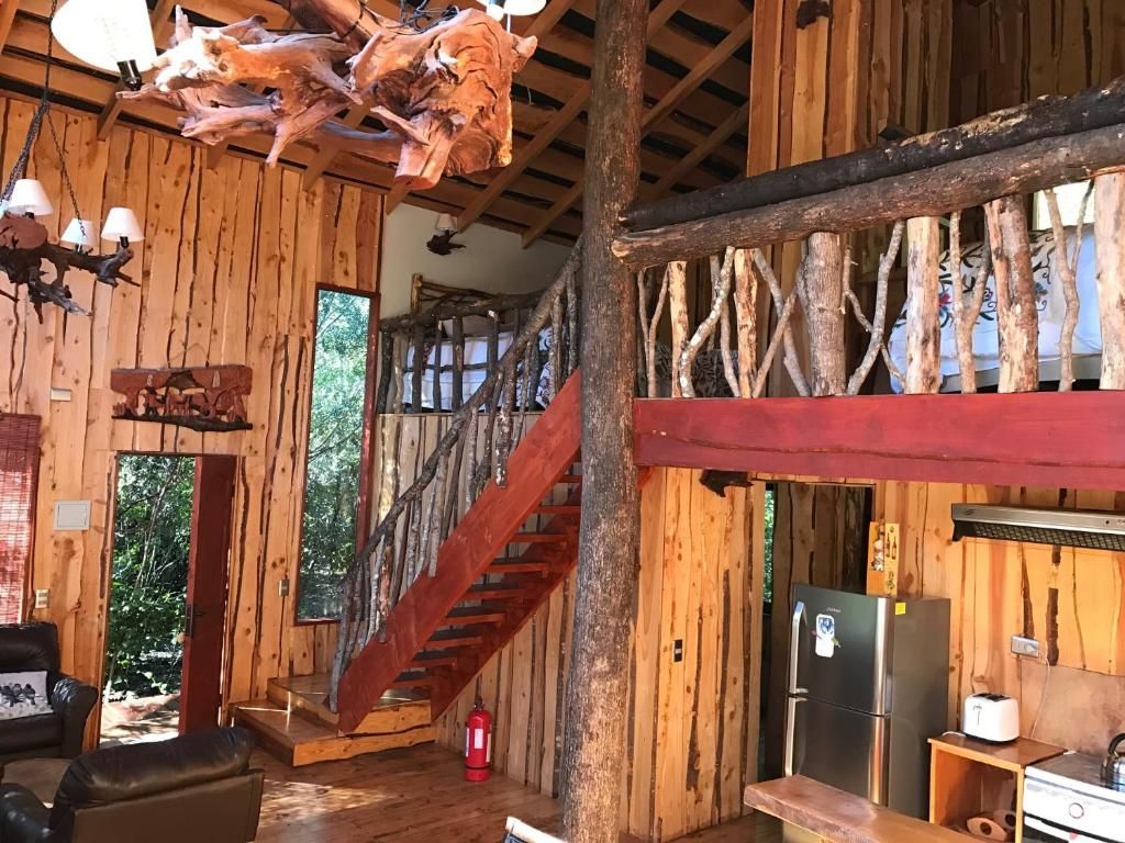 A rustic cabin interior with a wooden staircase, a dining area, and a kitchen.