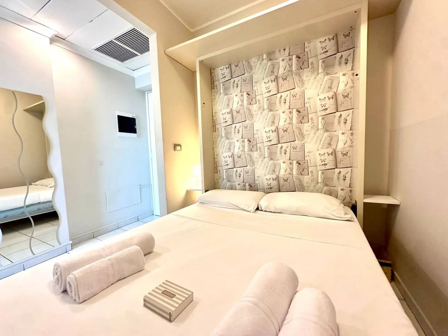 Hotellihuone, jossa on suuri sänky, seinä, jossa on perhoskuvituksia, ja kylpyhuone, joka näkyy avoimesta ovesta.