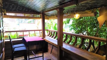 An outdoor seating area with wooden benches and tables, surrounded by a wooden railing, overlooking a lush garden.