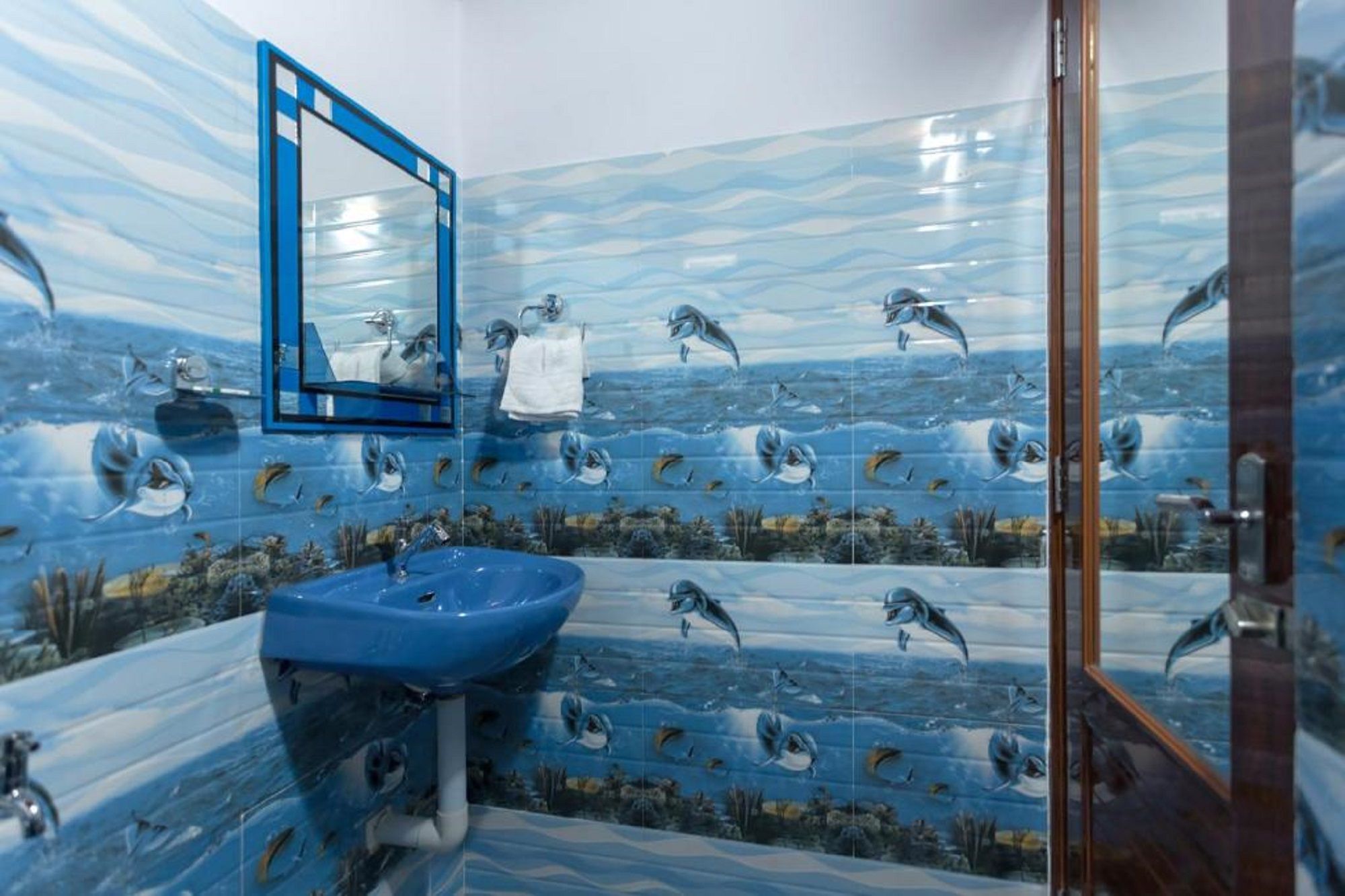 A bathroom with a blue sink, a mirror, and a tiled wall featuring dolphins.
