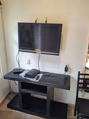 Ein Zimmer mit einem an der Wand befestigten Fernseher, einem Schreibtisch mit einem Computer und einem Stuhl.
