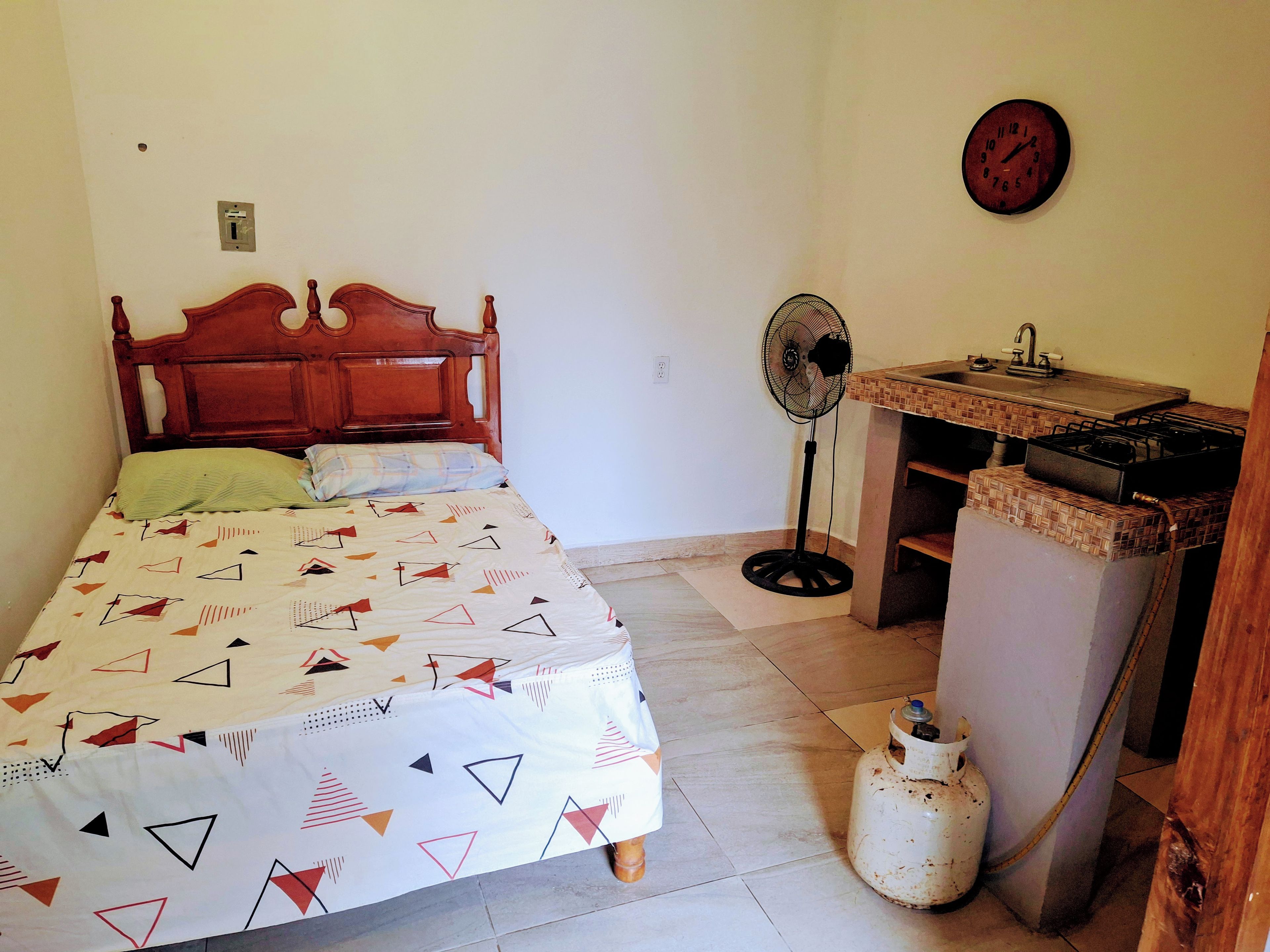 A bedroom with a wooden bed, a bedside fan, and a gas stove.