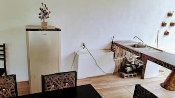 Cocina compacta con refrigerador, lavamanos y protector mural de azulejos.