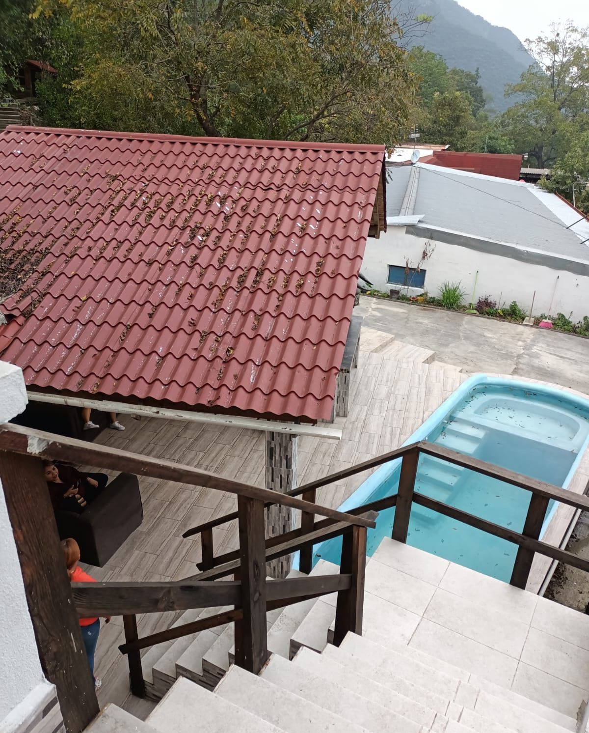A pool area with a red tiled roof, a staircase leading to a deck, and a view of the surrounding landscape.