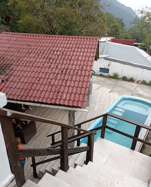 A pool area with a red tiled roof, a staircase leading to a deck, and a view of the surrounding landscape. - Miniquinta La Chula (Santiago)