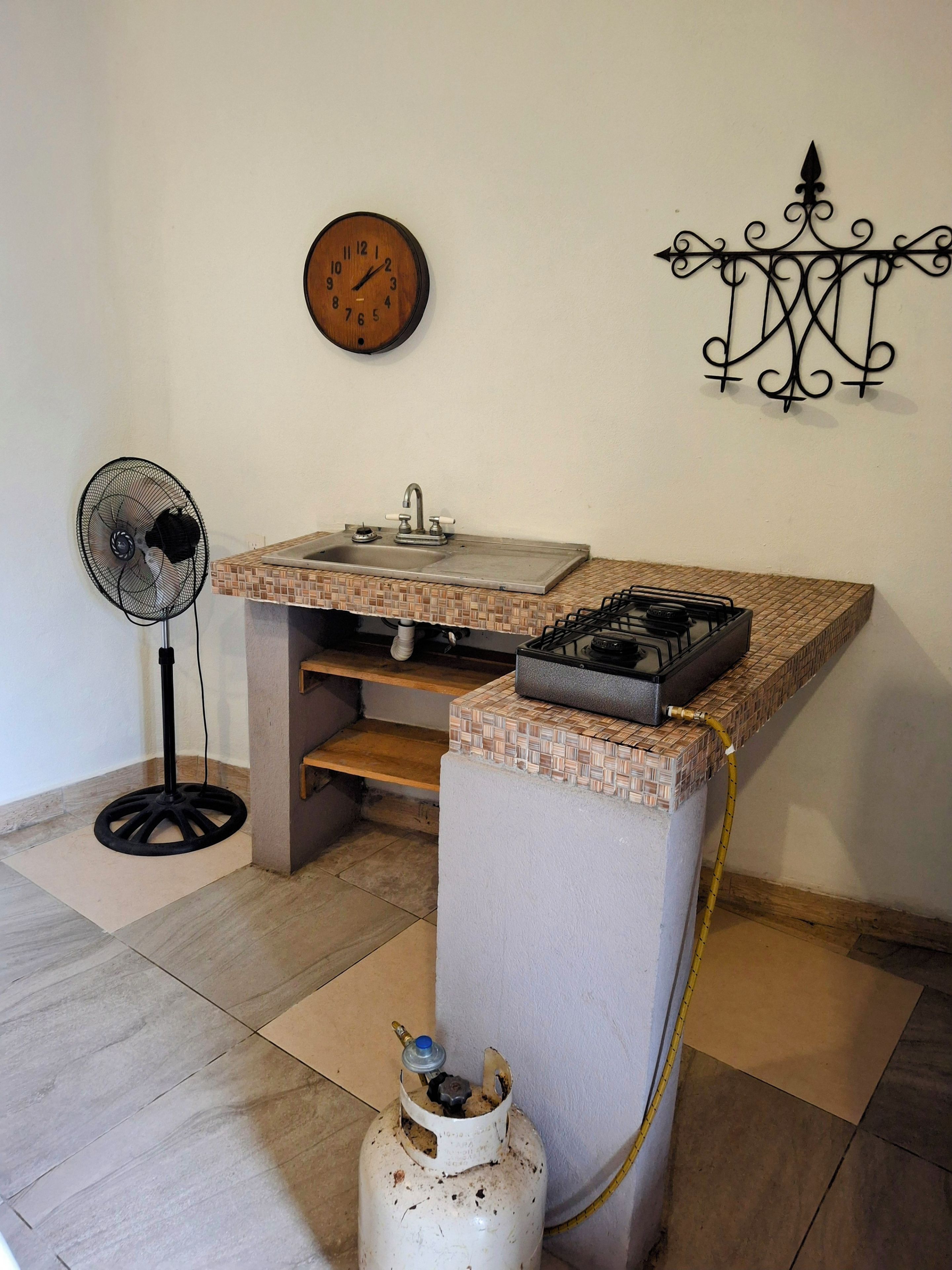 A compact kitchen with a sink, a gas stove, and a clock on the wall.
