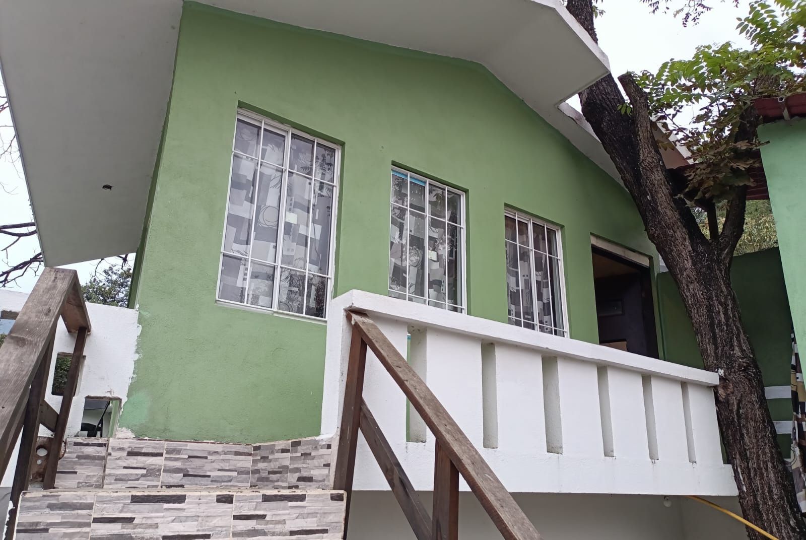 A green building with a white balcony and a staircase leading to the entrance.