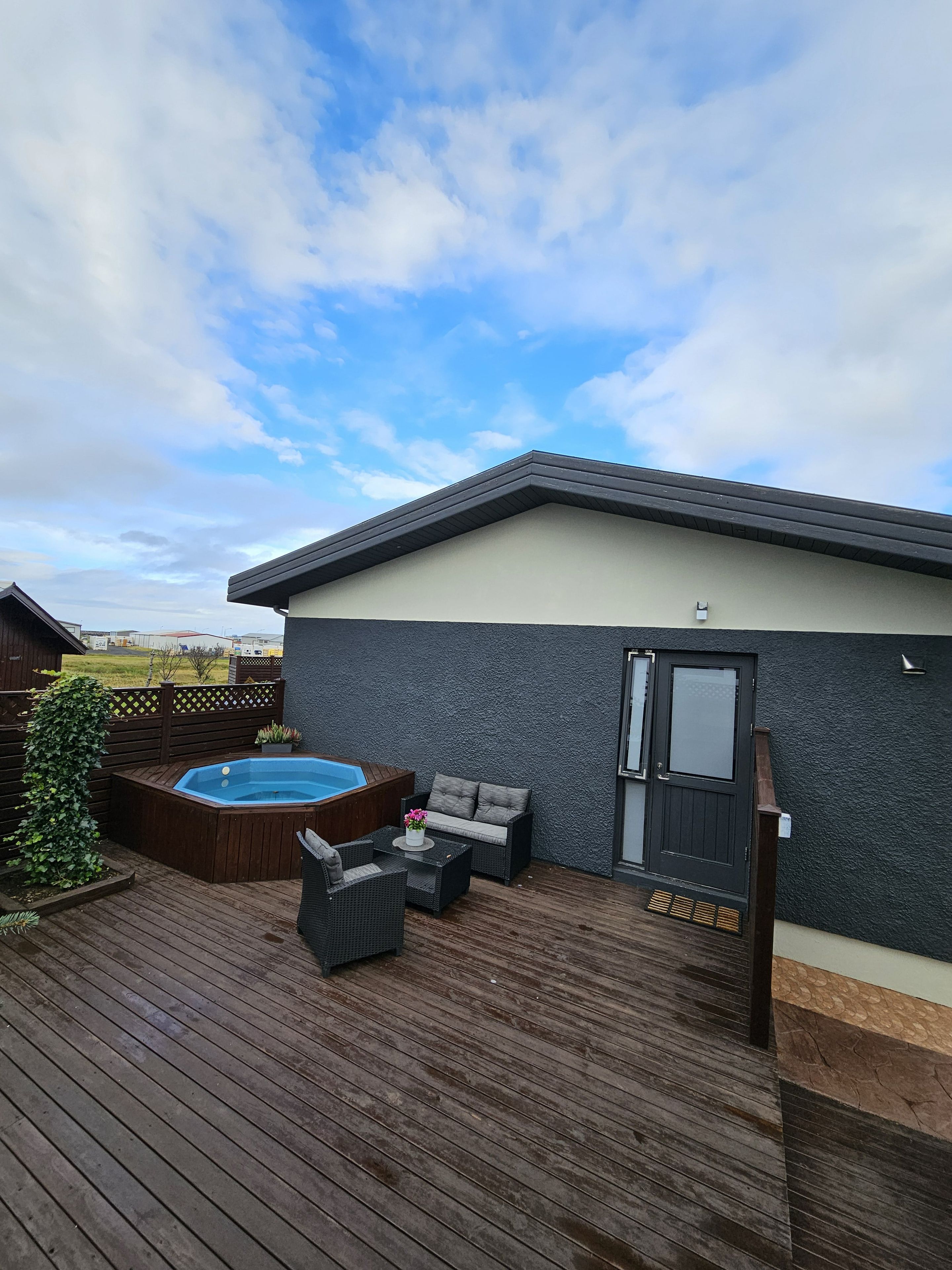 Eine Terrasse mit Whirlpool, Gartenmöbeln und einem Haus mit dunkler, strukturierter Fassade.