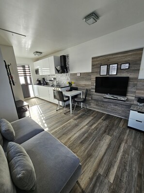 Ein zeitgemäßer Wohnbereich mit Sofa, Essplatz, Küche und einem an der Wand befestigten Flachbildfernseher.