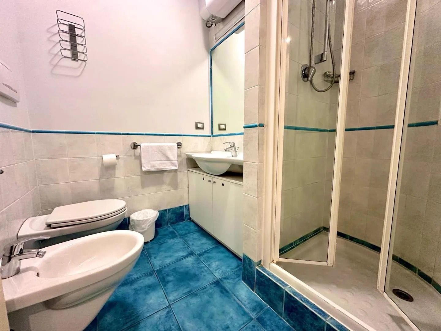 A bathroom with a toilet, bidet, sink, and a glass-enclosed shower area.
