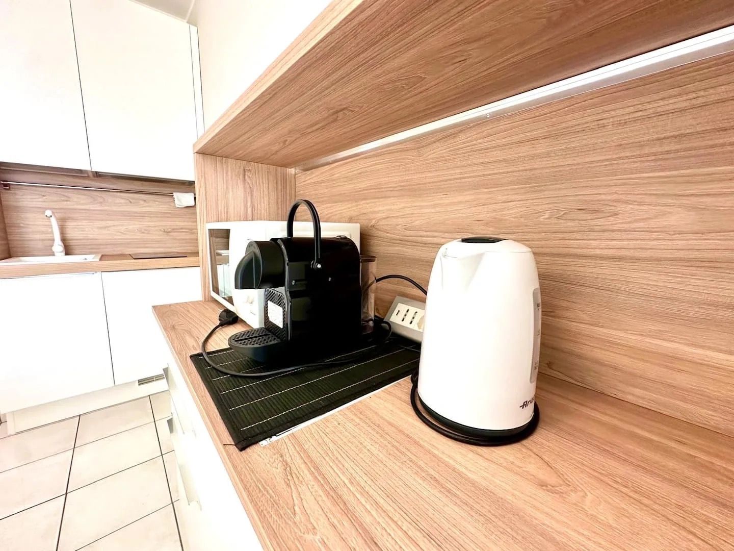 A modern kitchen with a coffee maker, a kettle, and a power strip on a wooden countertop.