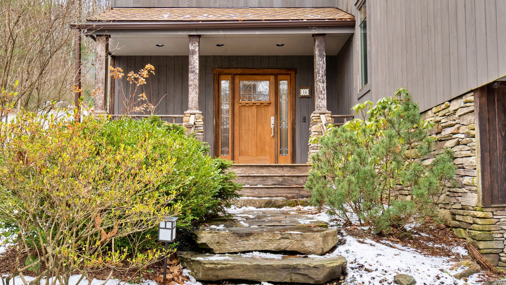 A house with a wooden front door, stone steps, and a porch with a railing.