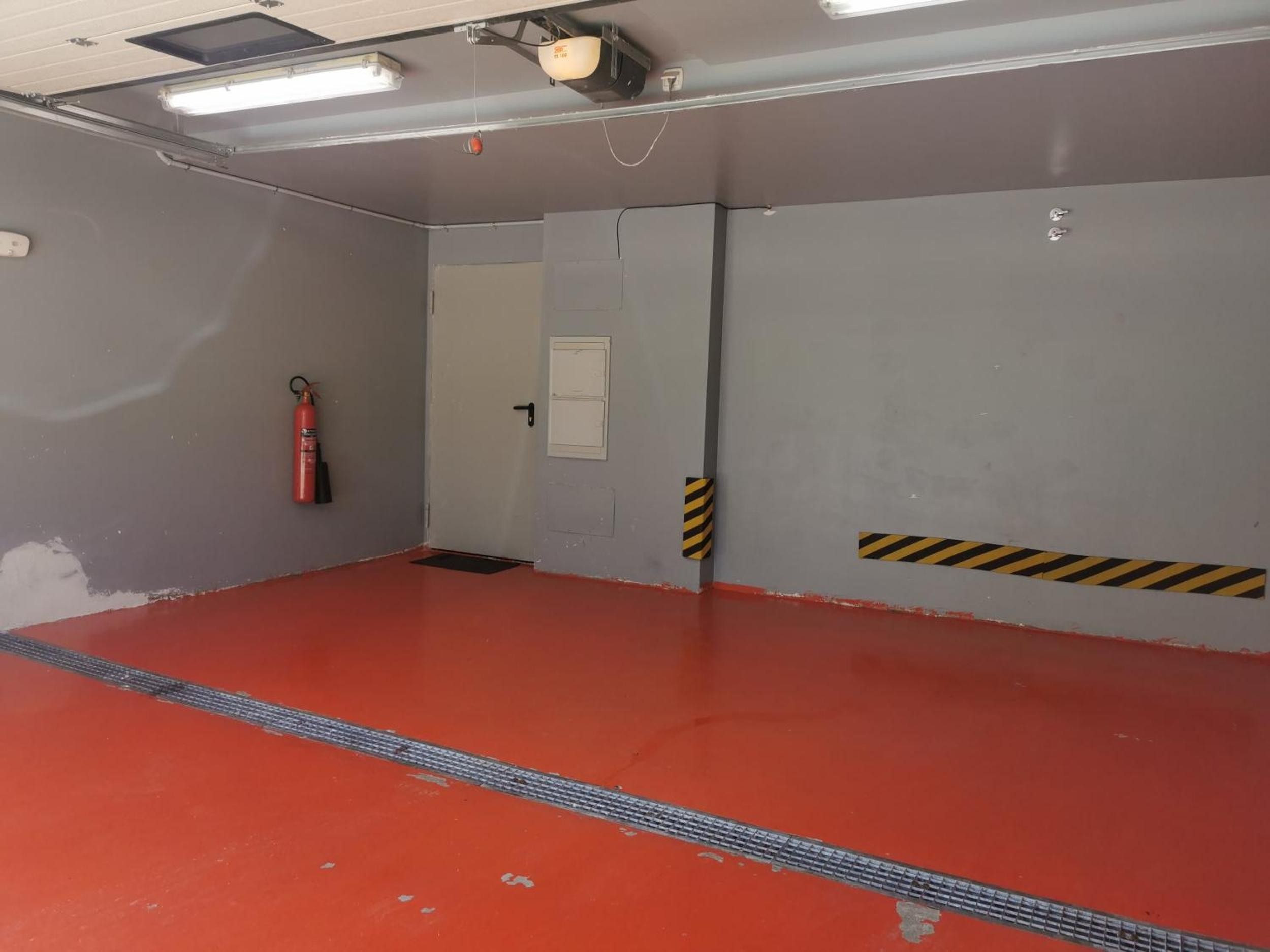 Una habitación con piso rojo, un extintor, una puerta y una lámpara en el techo.