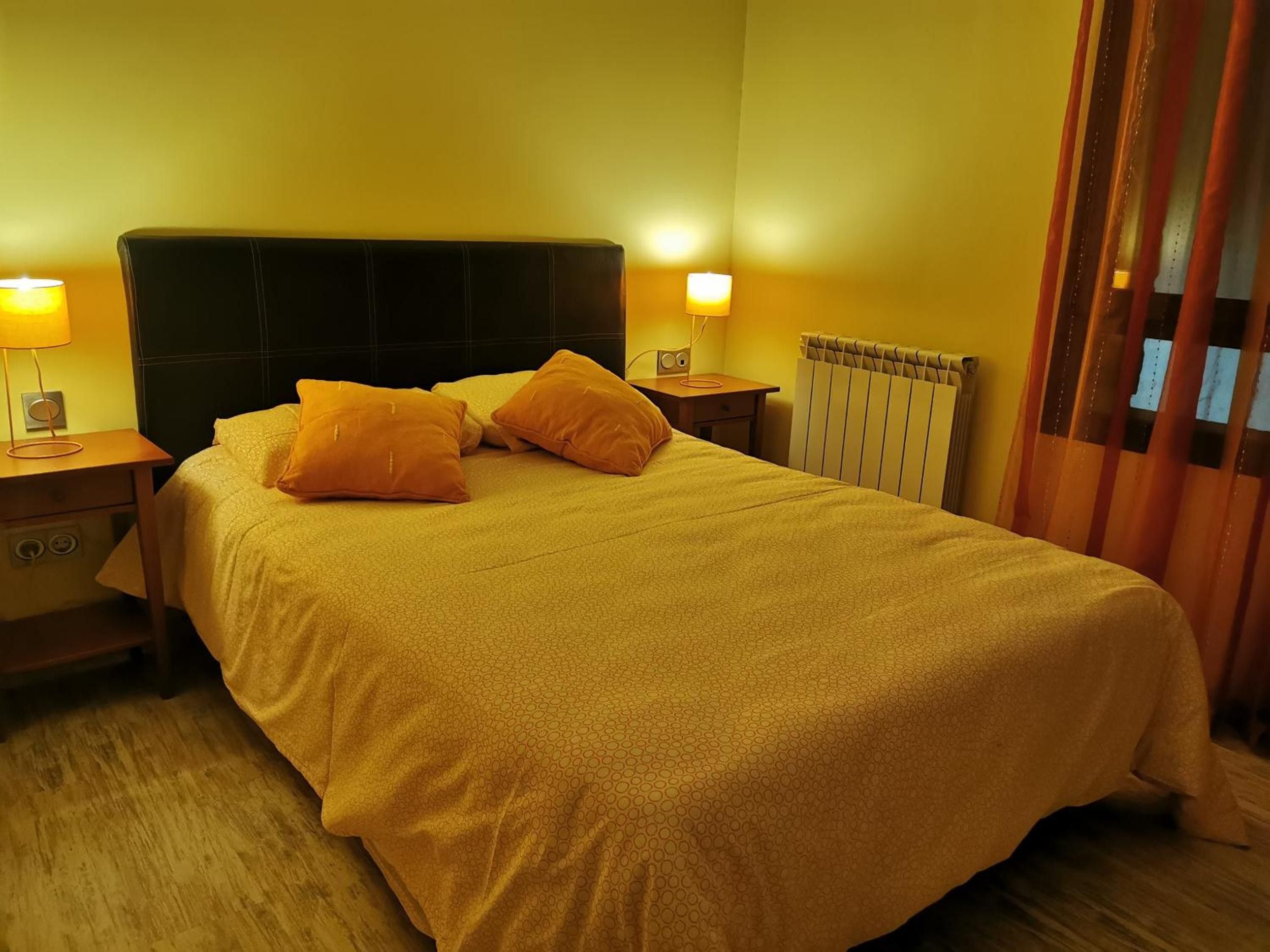 Une chambre d’hôtel avec un lit, deux lampes de chevet, un radiateur et une fenêtre avec des rideaux.