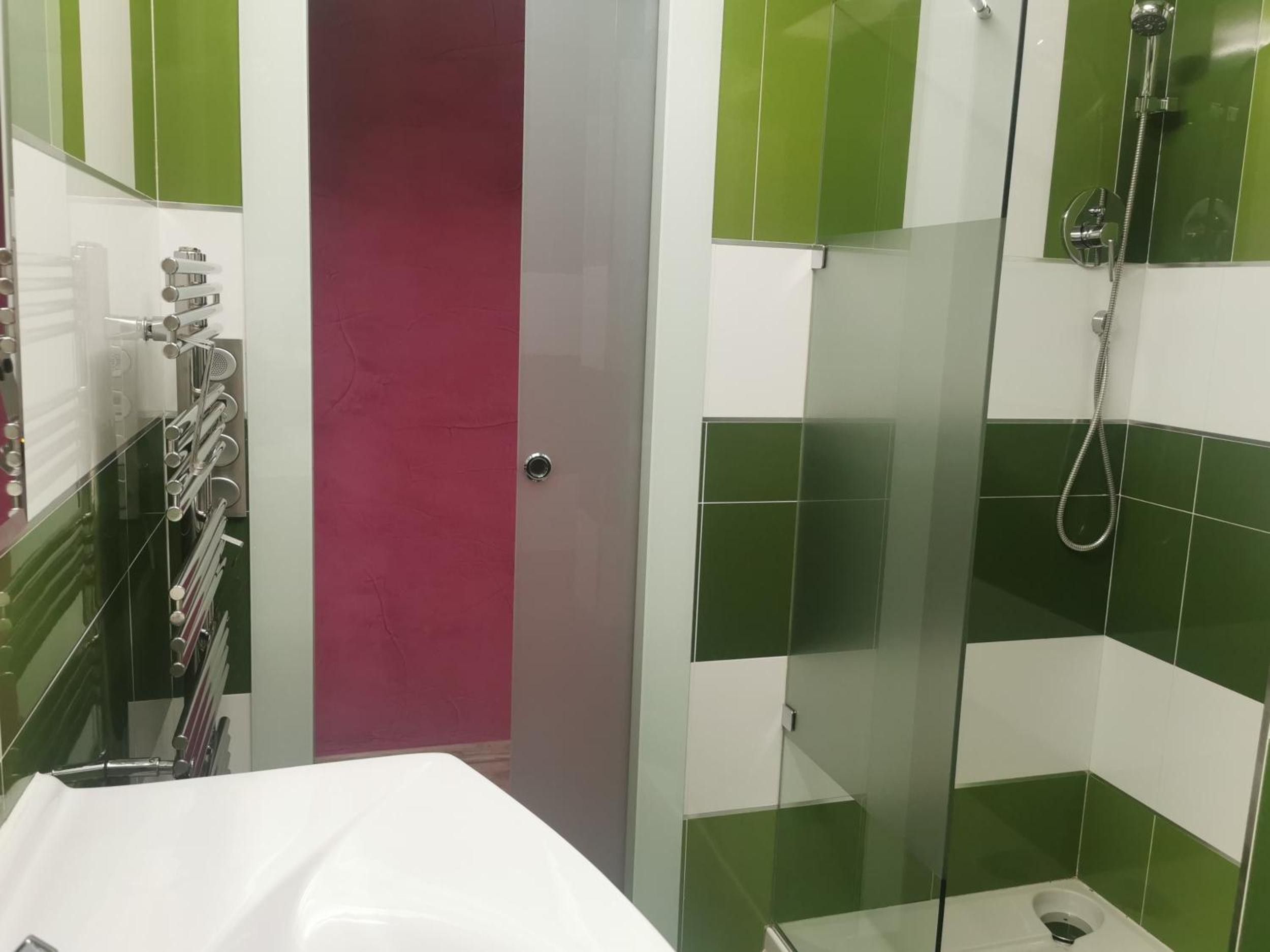 Un baño con cabina de ducha de vidrio, un lavamanos blanco y una puerta que da a una habitación rosa.