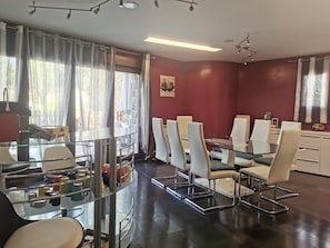 A modern conference room with a glass table and white chairs, a red accent wall, and a view of the outdoors through large windows.