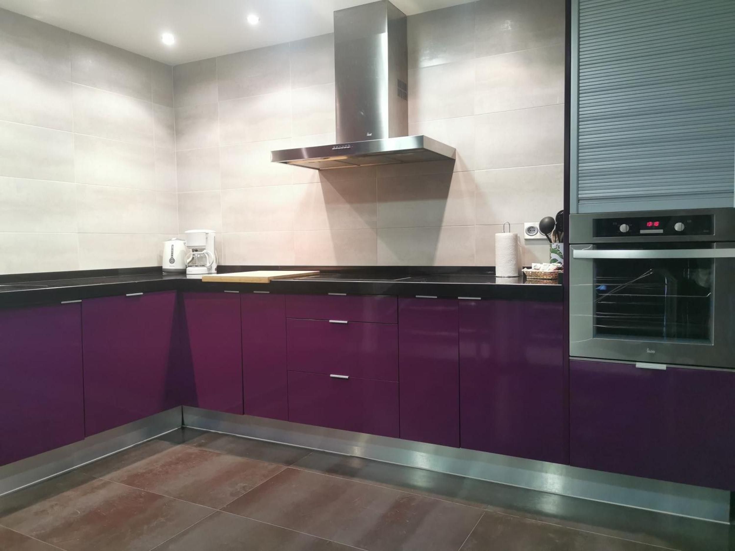 Une cuisine moderne avec des meubles de couleur violette, une hotte de cuisine en acier inoxydable, une machine à café et un four.