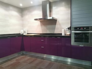 Una cocina moderna con armarios morados, una campana extractora de acero inoxidable, una cafetera y un horno.