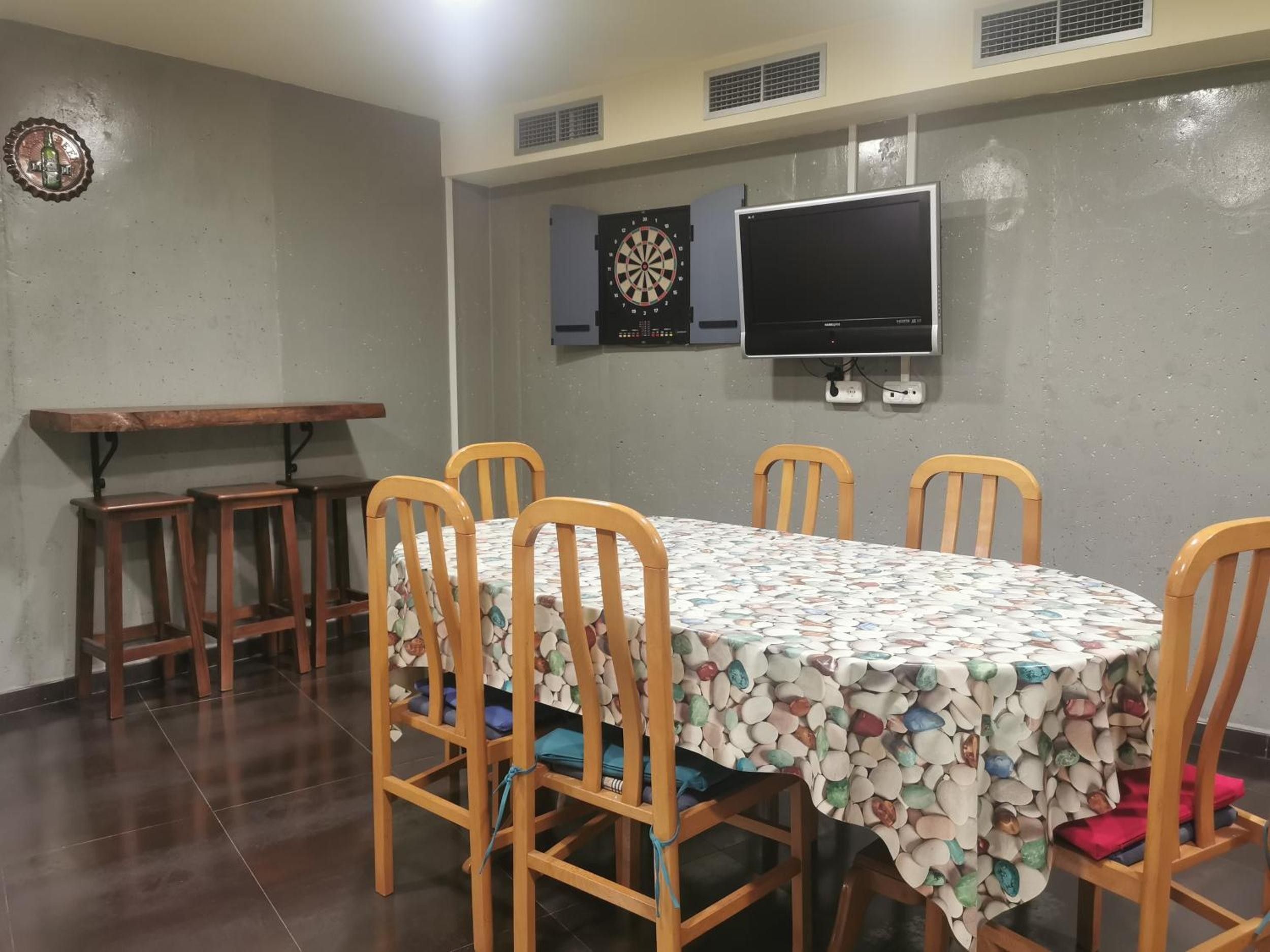 Un espace repas comprenant une table, des chaises, un jeu de fléchettes et un téléviseur.